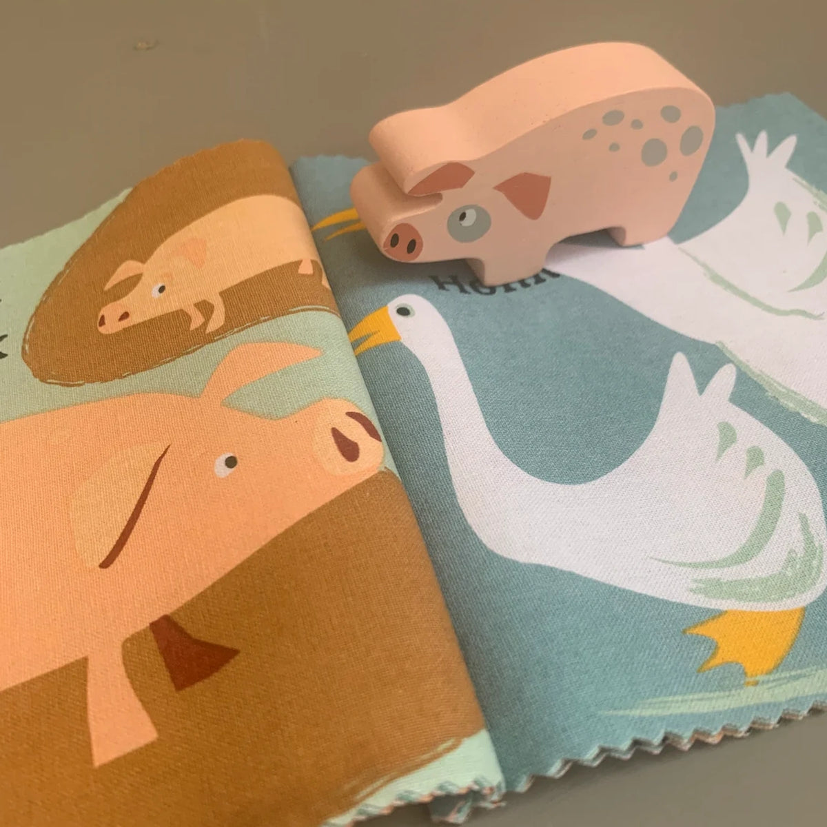 Wooden pig toy standing on an open cloth book illustrating pigs and geese.