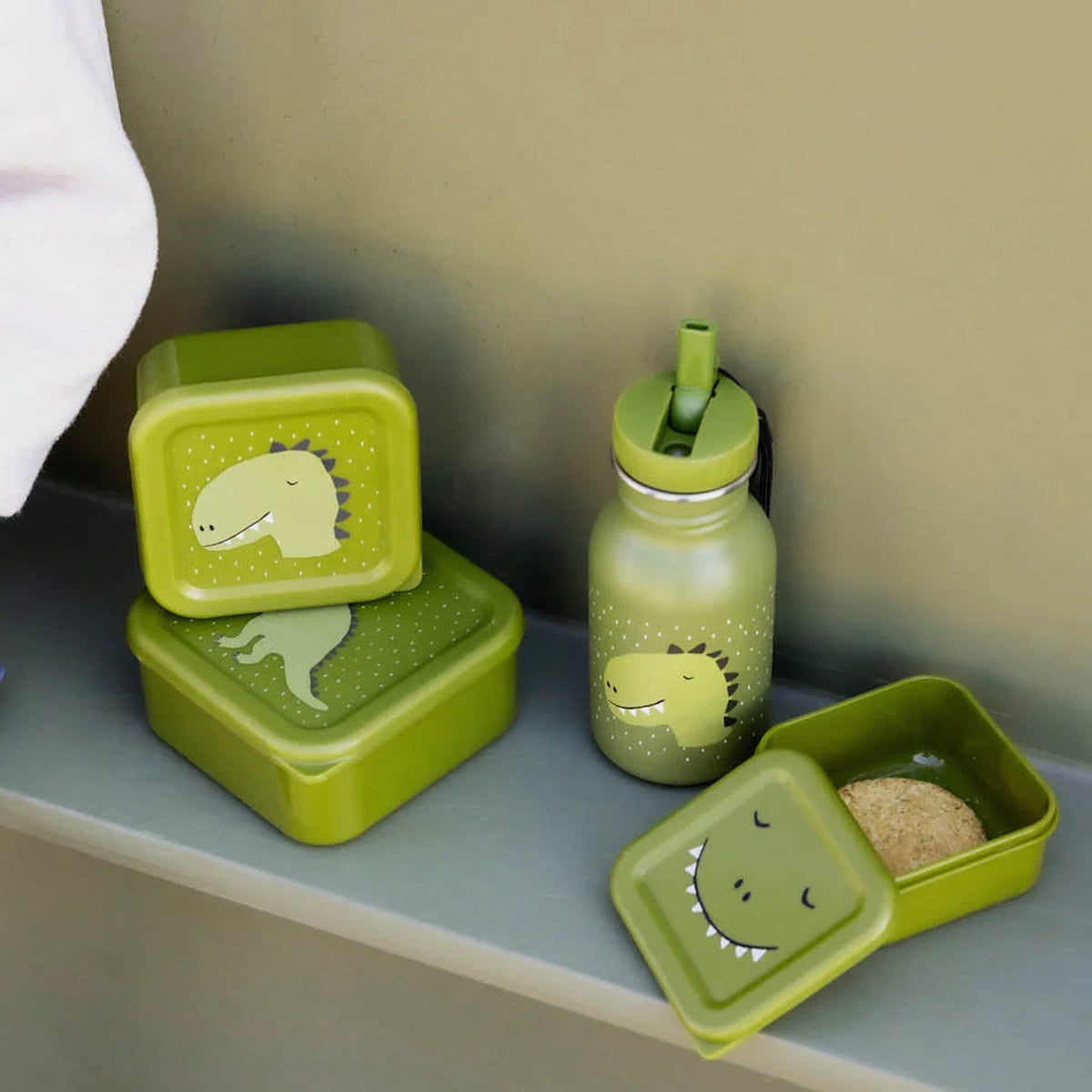Green kids water bottle next to matching stacked and open green dinosaur-themed lunch boxes.