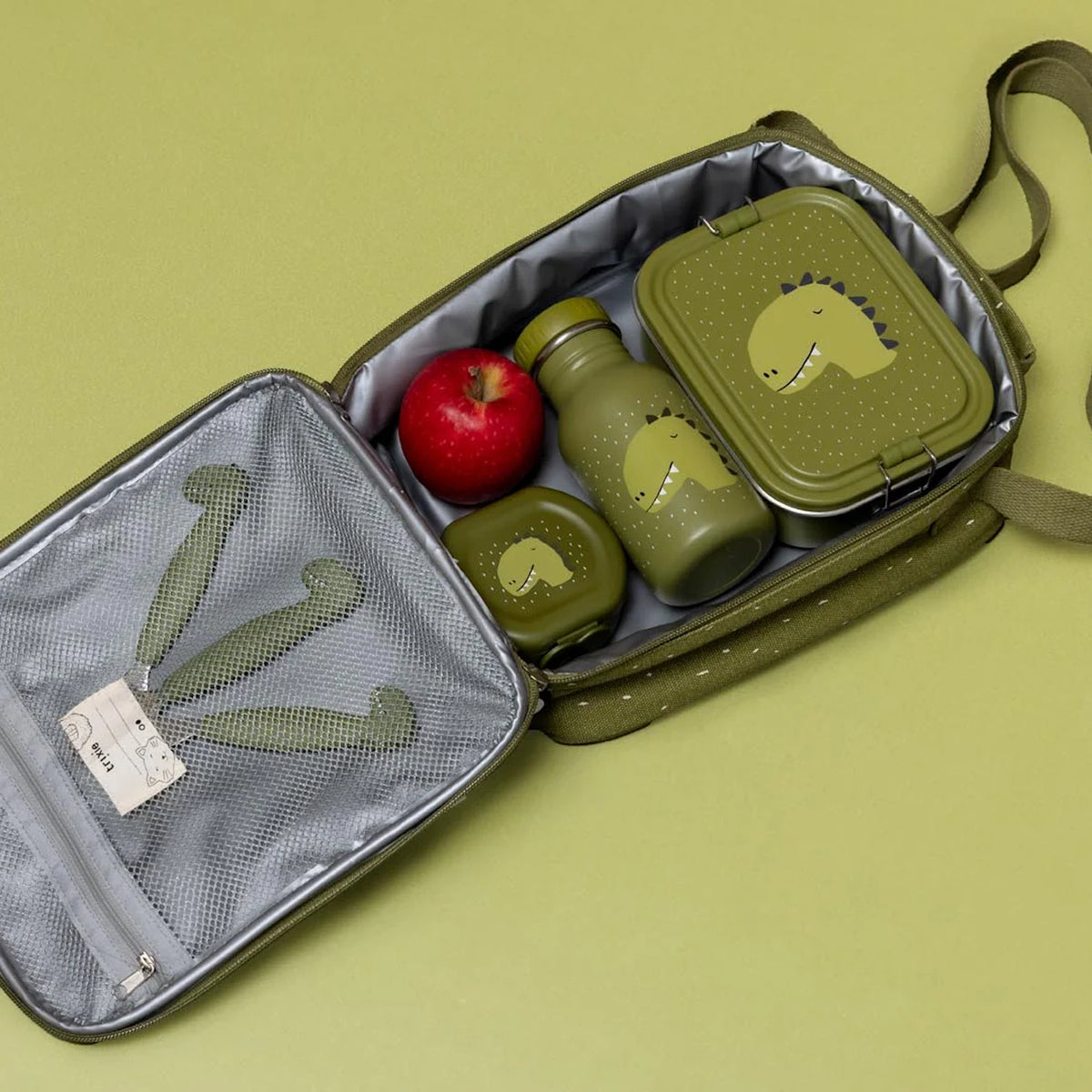 An open green lunch bag packed with a red apple and a matching dinosaur-themed water bottle and lunch box.