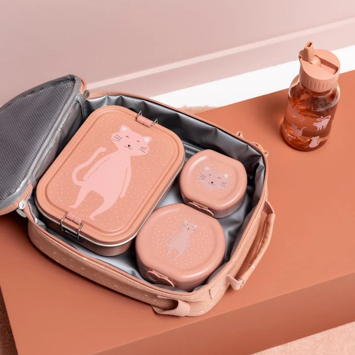 An open pink lunch bag filled with three pink cat-themed lunch containers next to a matching water bottle.