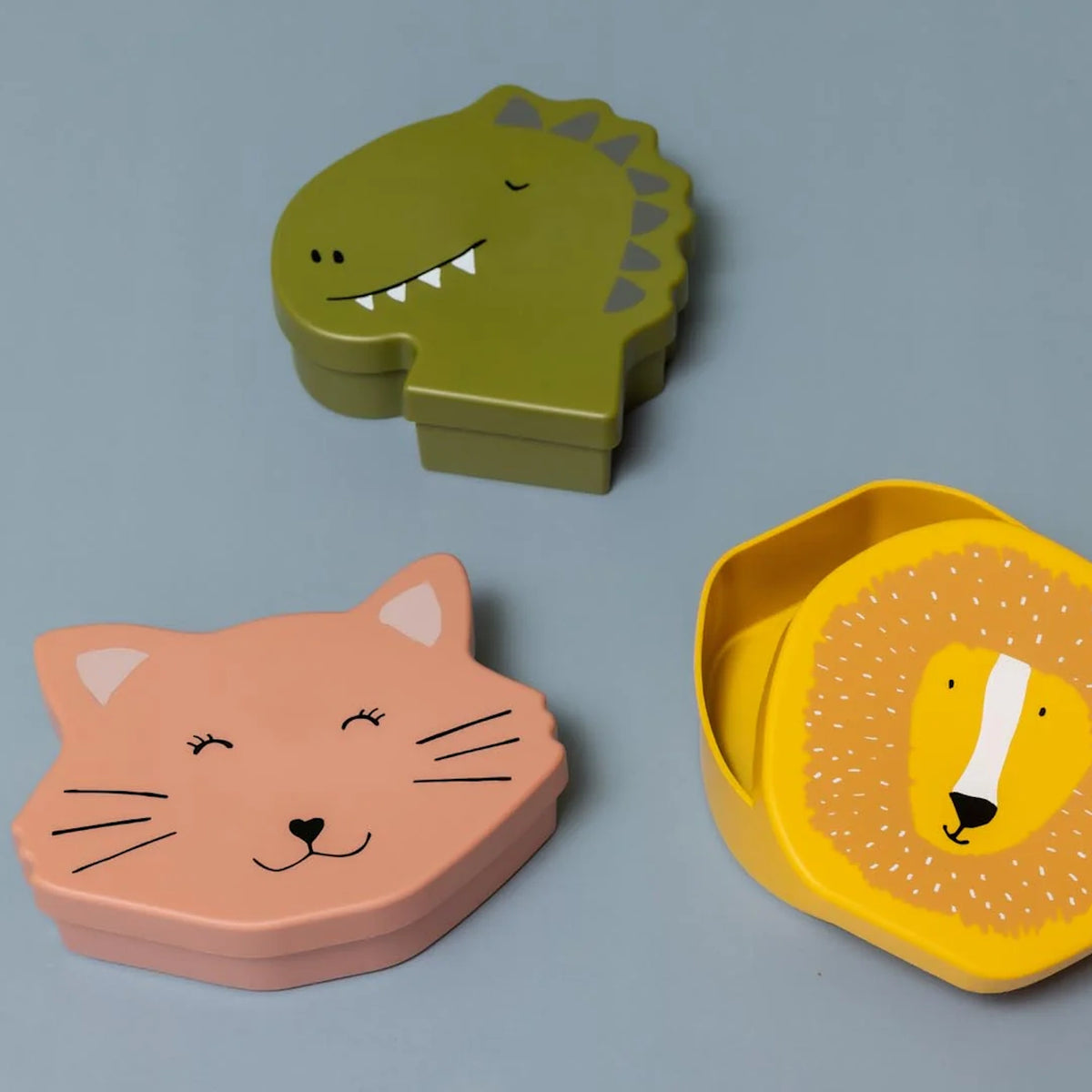 Three animal-shaped lunch boxes (dinosaur, cat, and lion) arranged on a grey background.