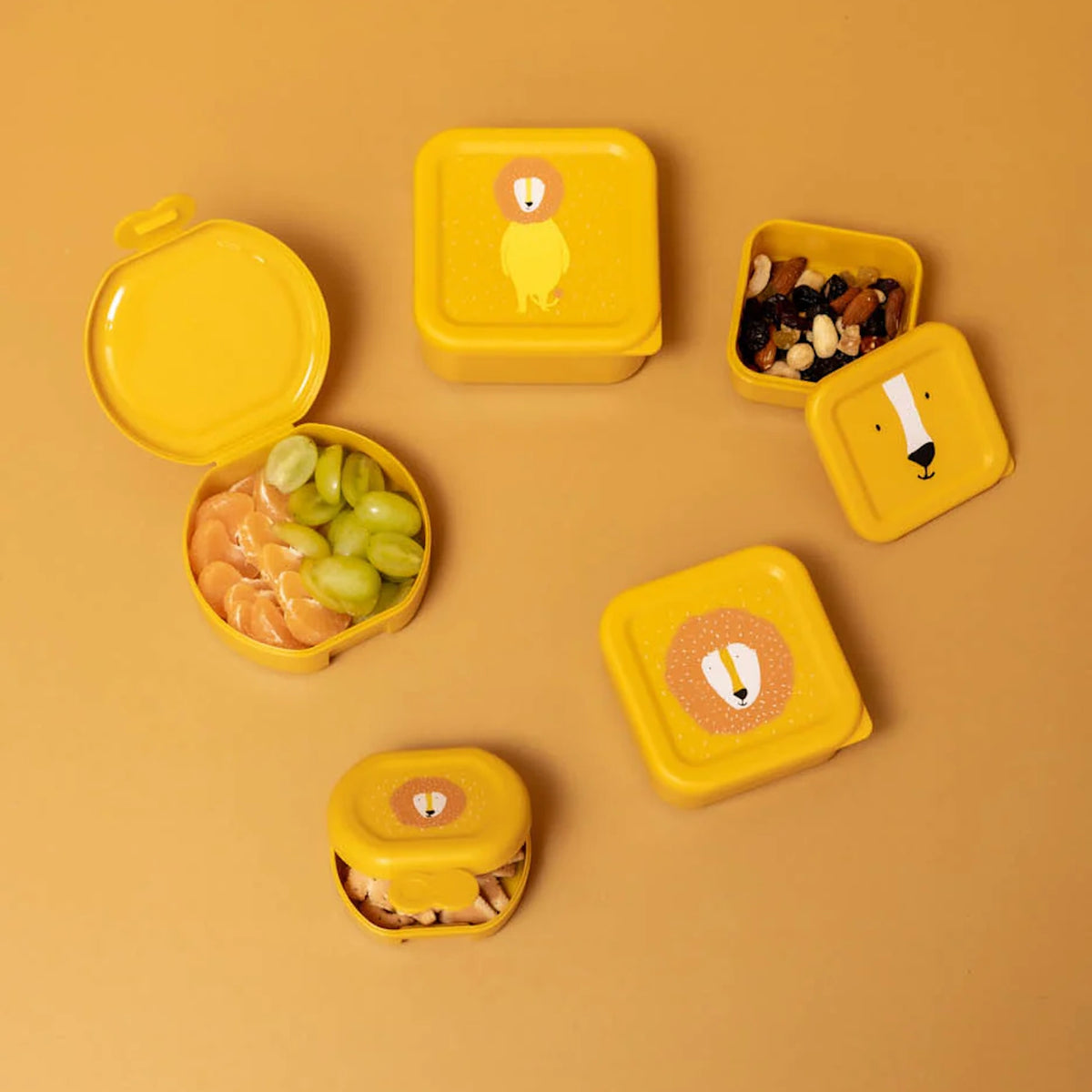 An assortment of yellow lion-themed snack containers, some open with fruit and nuts, on a yellow background.