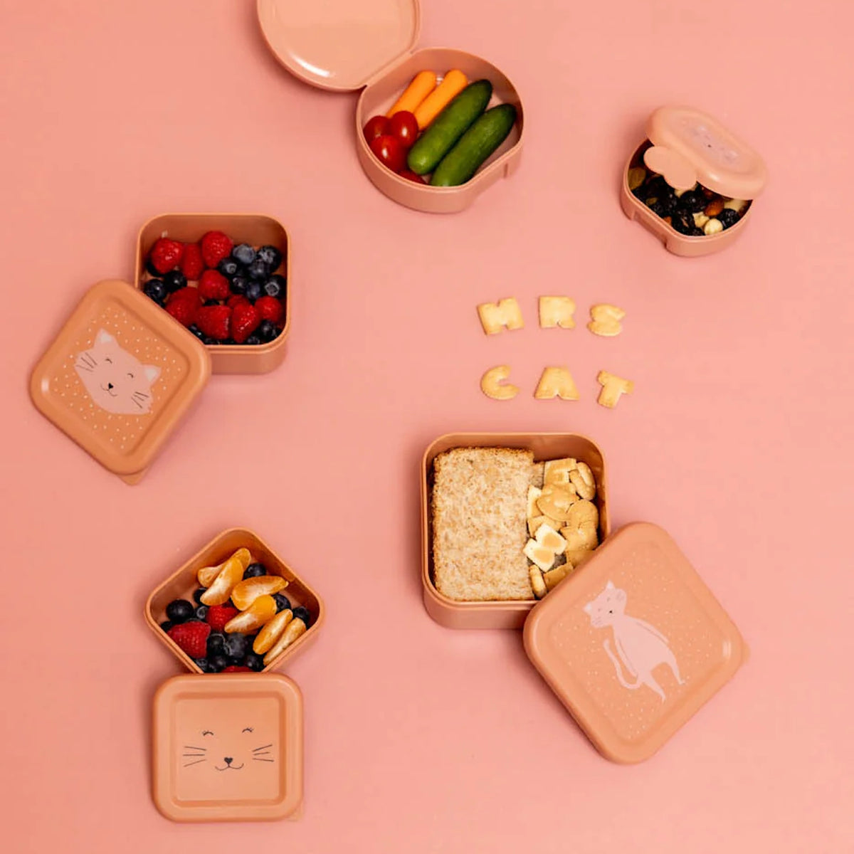 Open pink cat-themed snack boxes filled with berries, vegetables, and a sandwich on a pink background.