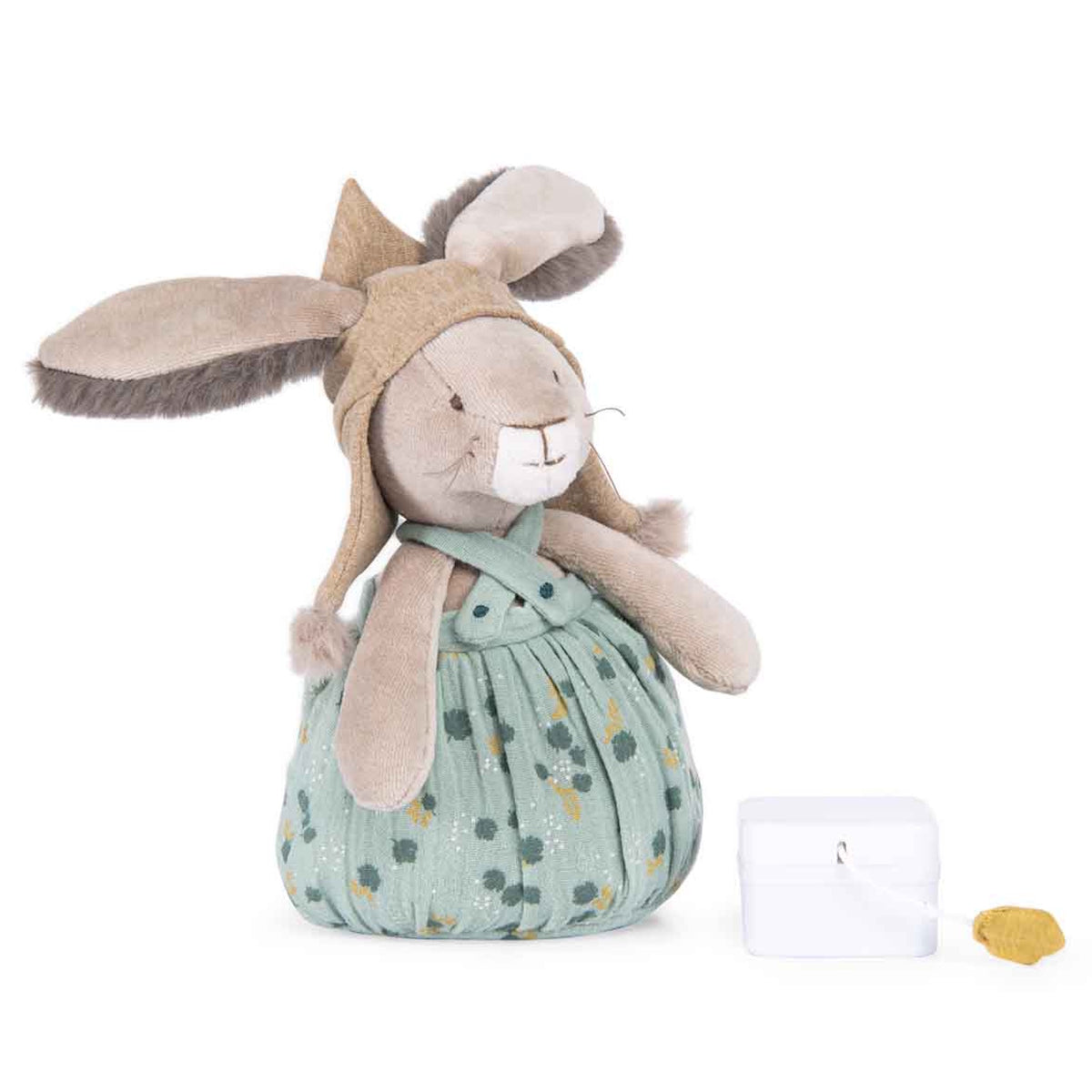 Plush rabbit toy wearing a pointed hat and floral overalls, standing next to a small white music box.