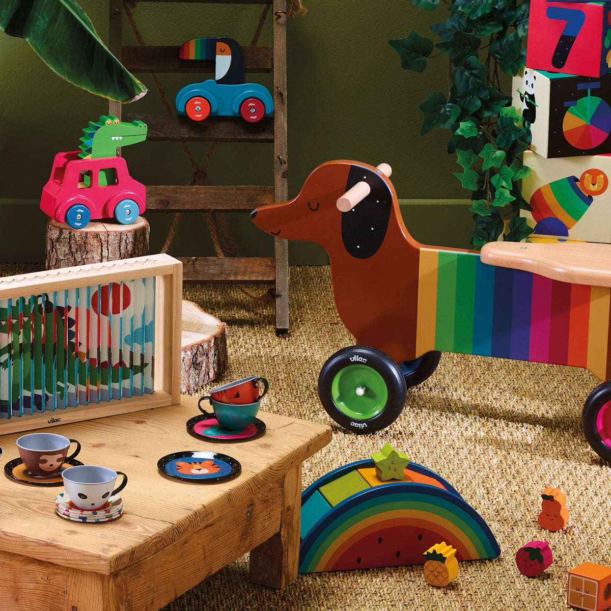 Colorful wooden children's toys including a rainbow dachshund rider, animal tea set, and blocks on a natural rug.
