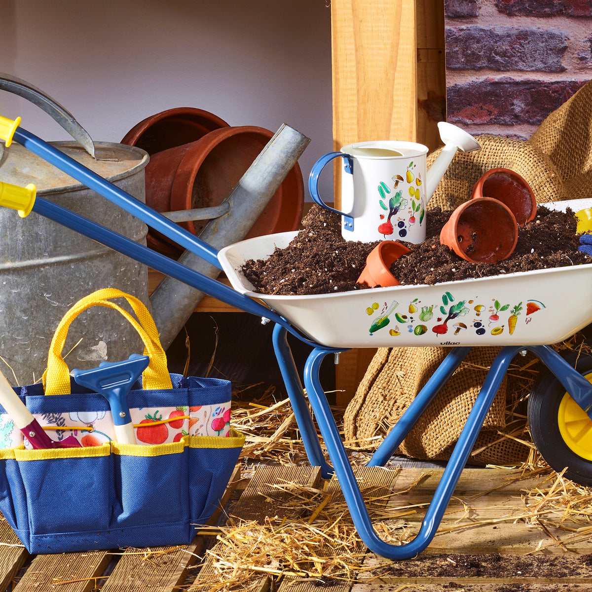 Kids colorful wheelbarrow set with watering can, pots, and garden tool tote bag filled with soil and straw.