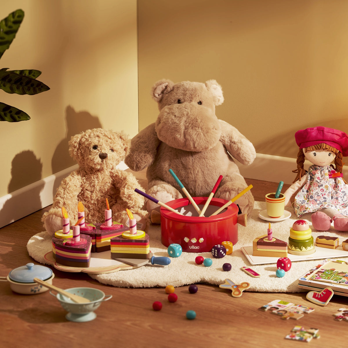 Vilac kids toy setup with plush toys, wooden birthday cake, toy drum, and play food on a rug.