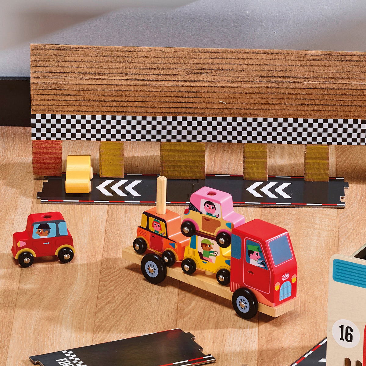 Wooden toy car carrier truck transporting colorful cars on a play track with a checkered racing finish line.