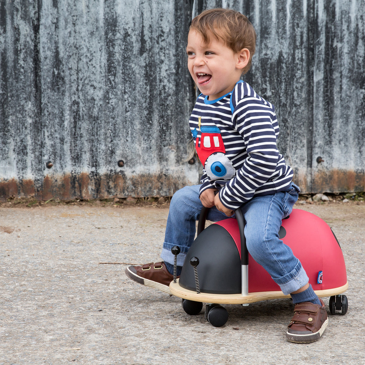 Smiling toddler riding a ladybird Wheely Bug ride-on toy outdoors.
