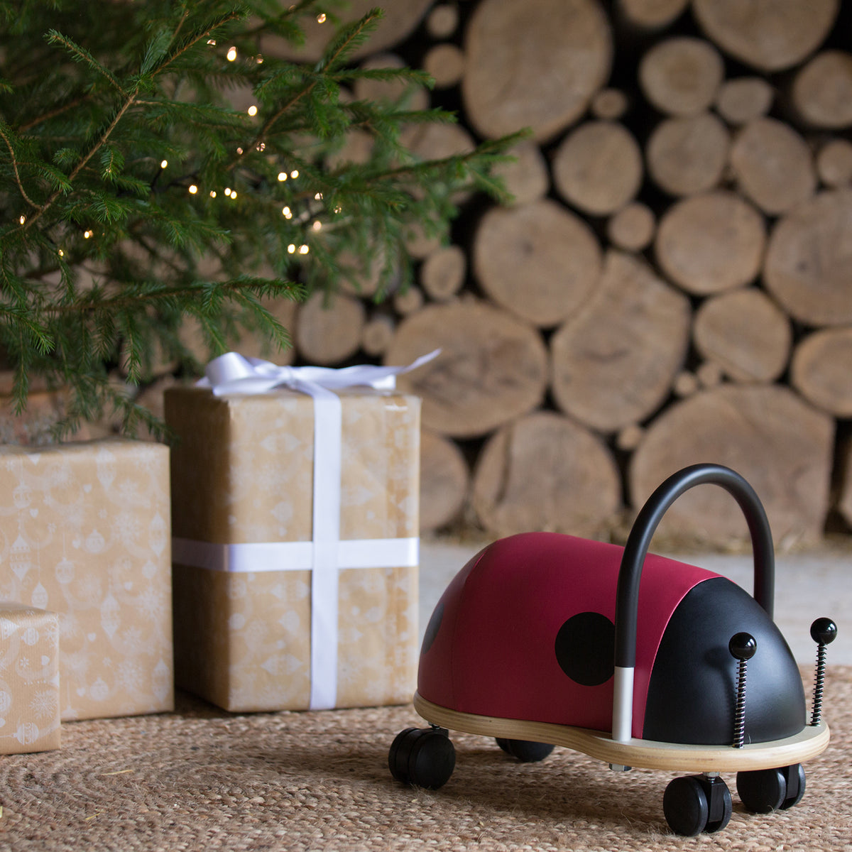Red ladybird Wheely Bug ride-on toy next to Christmas presents under a lit tree.