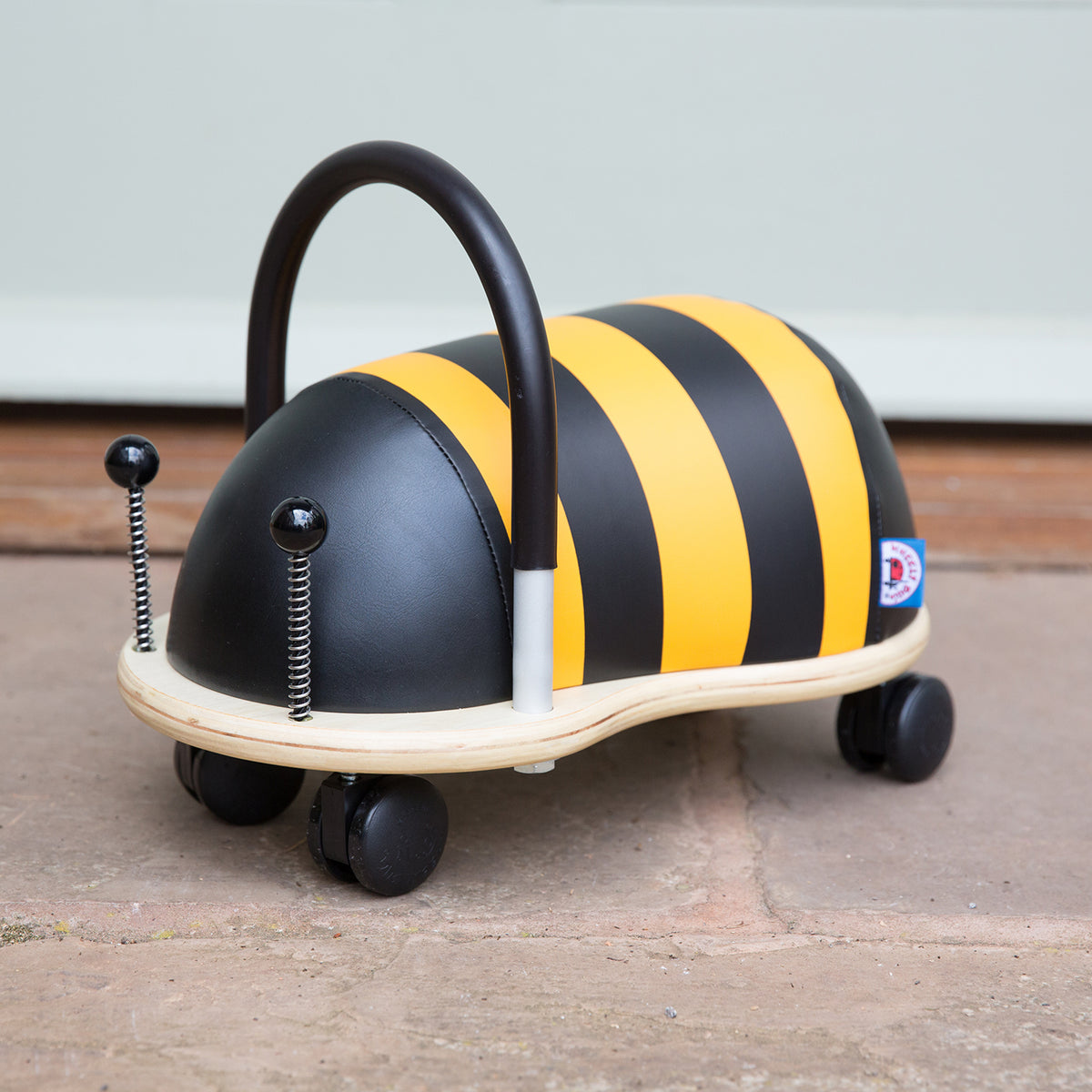 Plush bumblebee Wheely Bug ride-on toy with wheels and black handle on a stone patio.