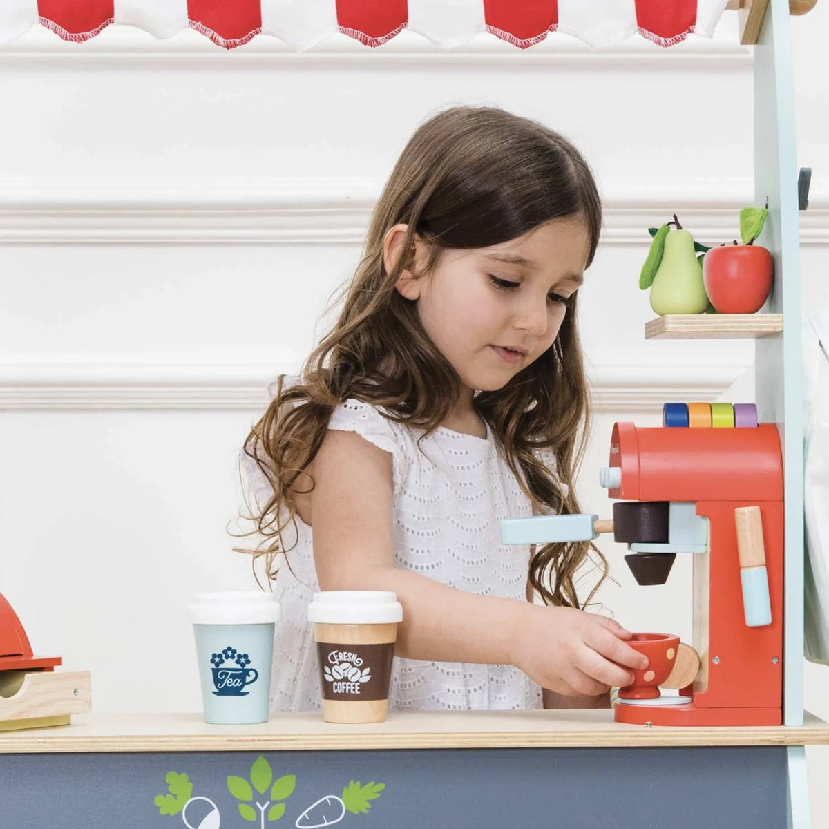 A young girl playing with the wooden toy coffee machine and cup at a market stall.