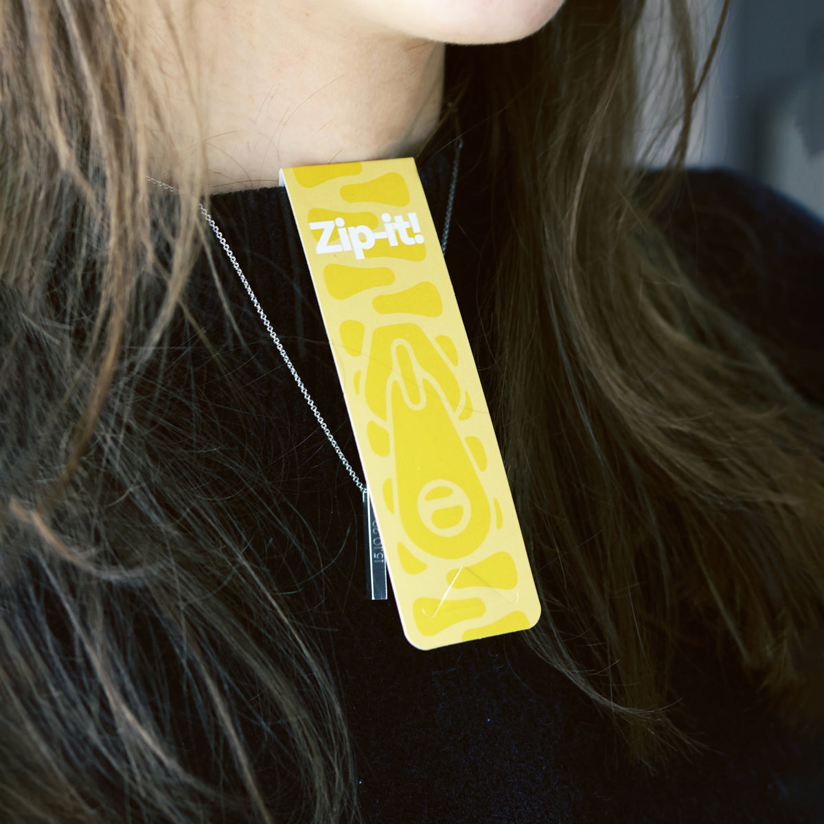 A yellow Zip-it! game card clipped to the collar of a black sweater worn by a person.