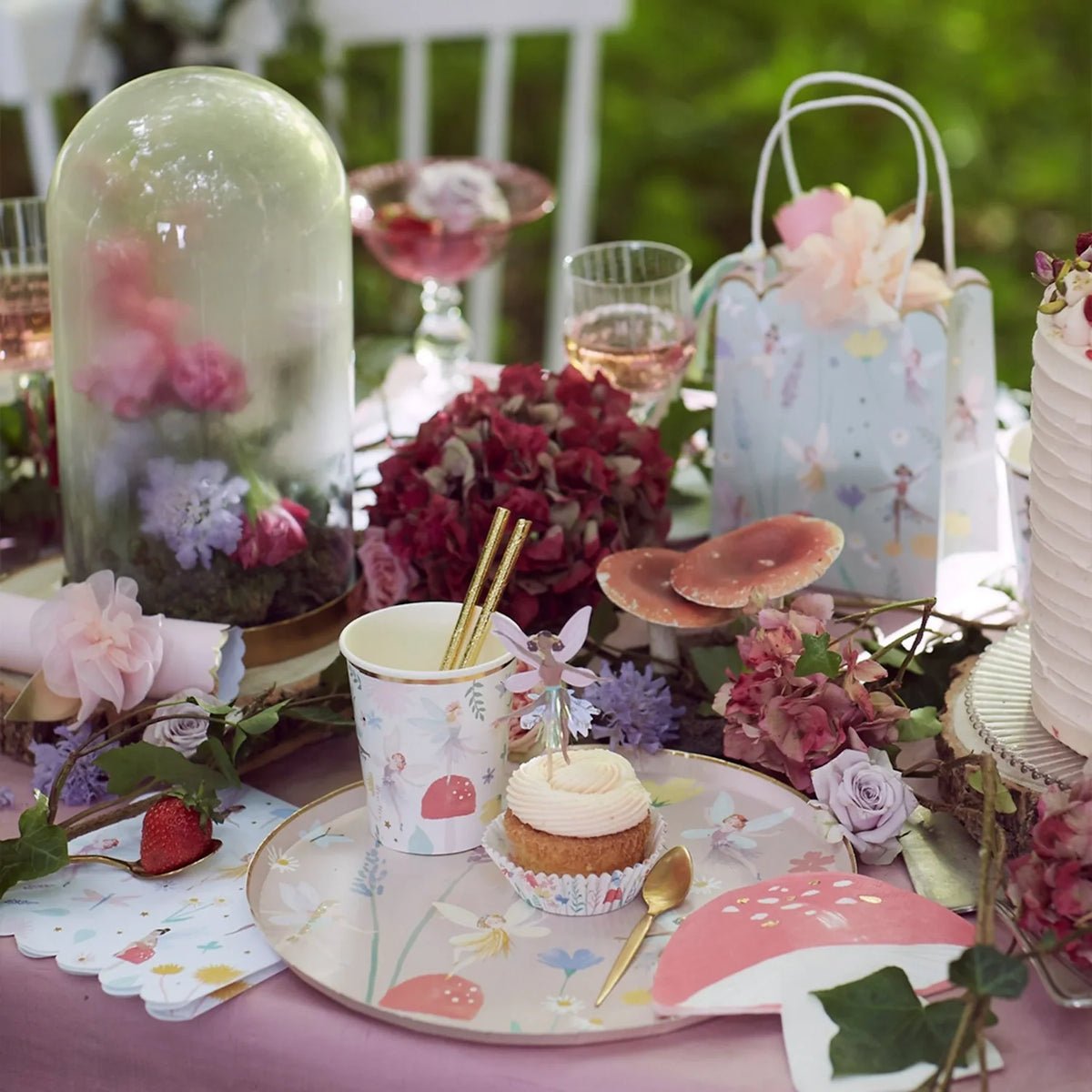 Fairy party table set with fairy cups, plates, napkins, cupcake and party bag among flowers