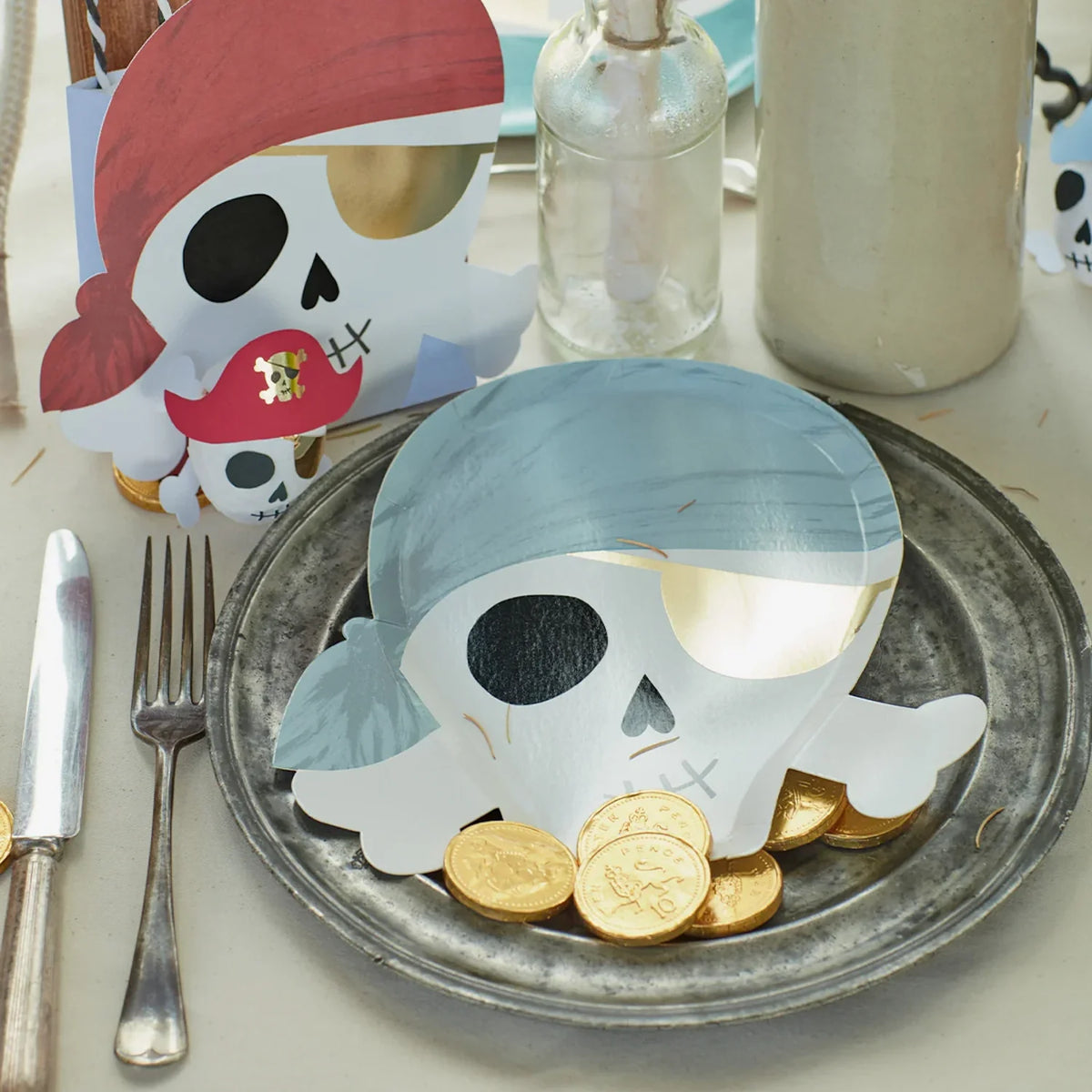 Children's party table laid with pirate skull plates, cups and gold coins