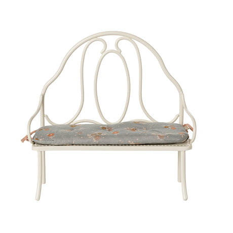 A front-facing view of the Maileg vintage-style bench in off white, highlighting its intricate metalwork and attached blue floral cushion.