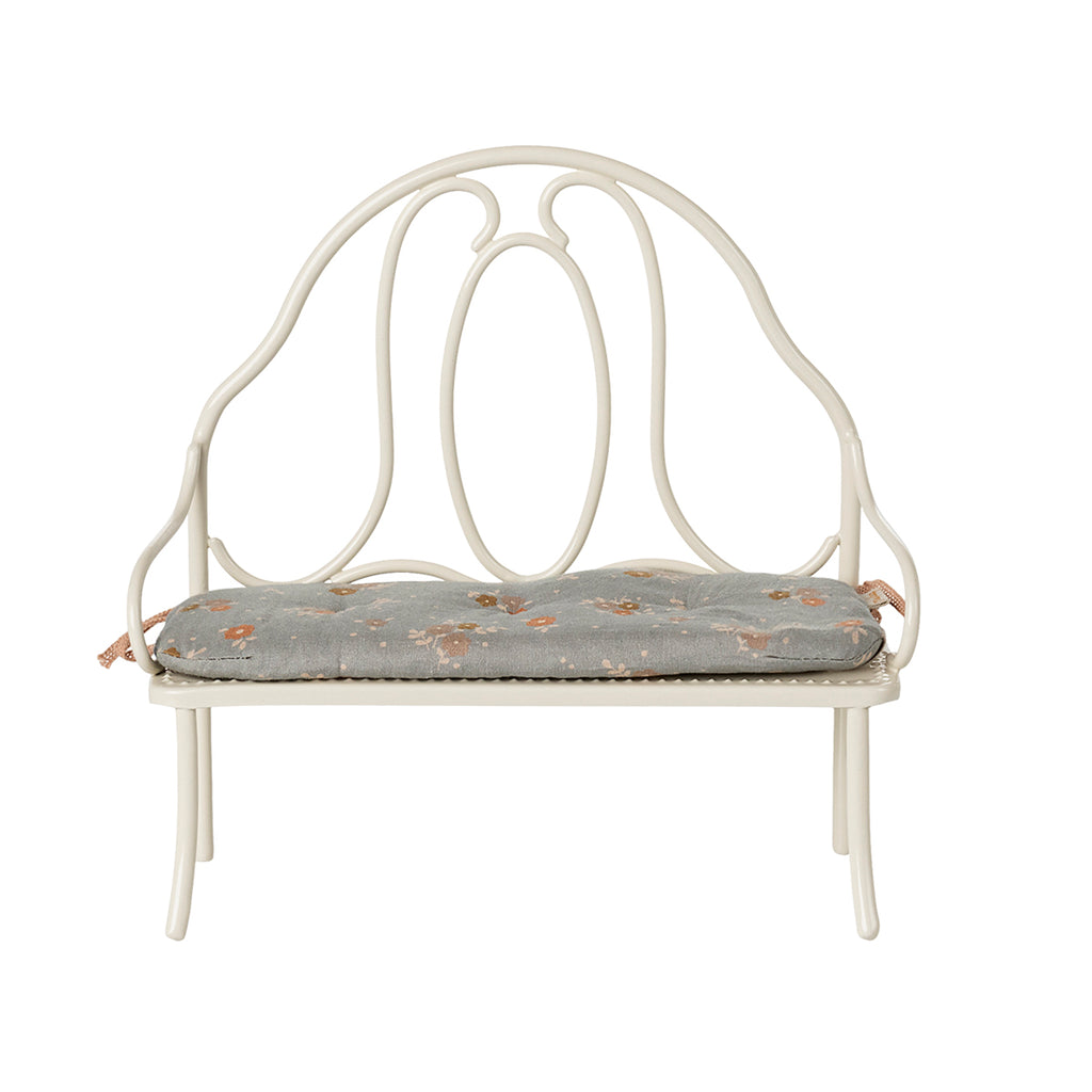 A front-facing view of the Maileg vintage-style bench in off white, highlighting its intricate metalwork and attached blue floral cushion.