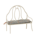 A charming Maileg vintage-style metal bench in off white, featuring a delicate blue floral-patterned cushion tied to the back poles.
