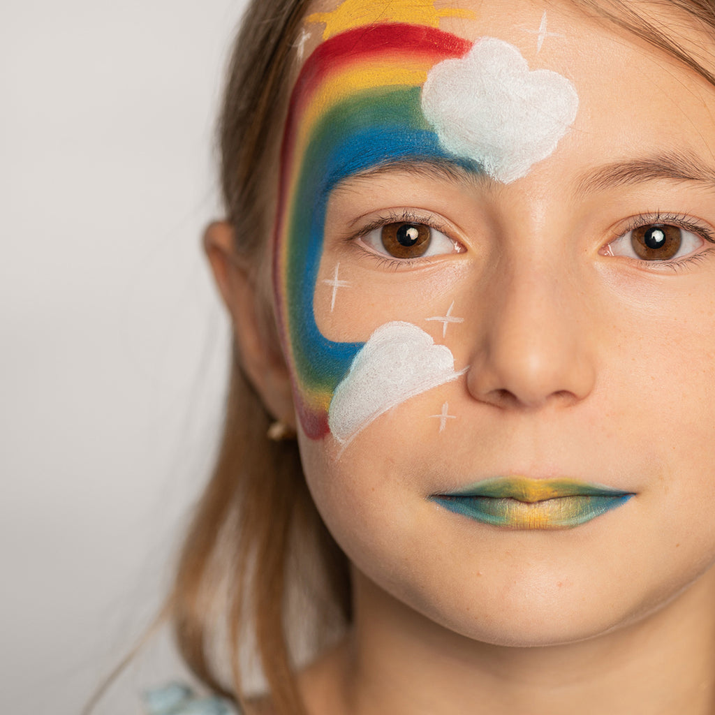 A close-up of a child with a rainbow and cloud-themed face paint design, featuring vibrant colours and white cloud details.