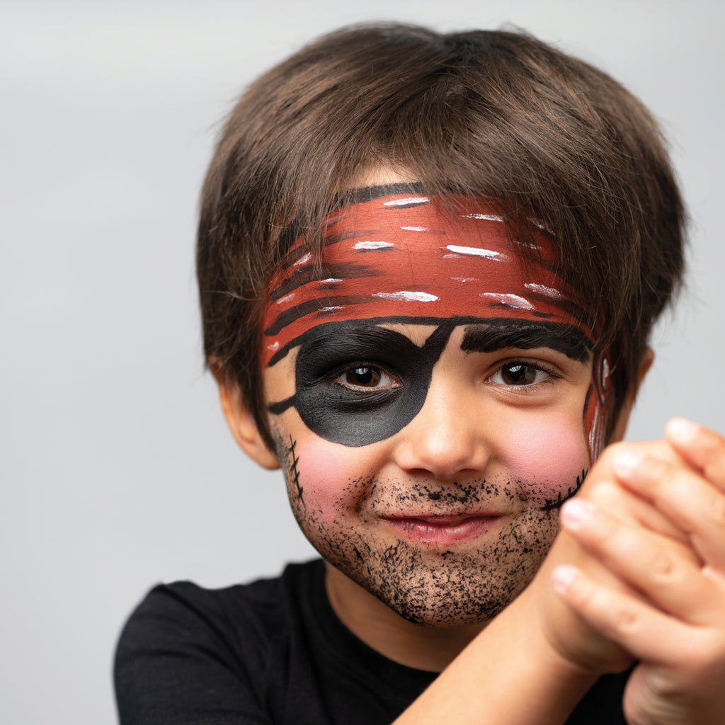 A smiling child with a pirate face paint design, featuring a red bandana, black eye patch, and beard details.
