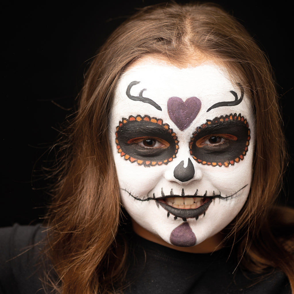 A close-up of a child wearing sugar skull-inspired face paint with black eye details, white face paint, and decorative accents.