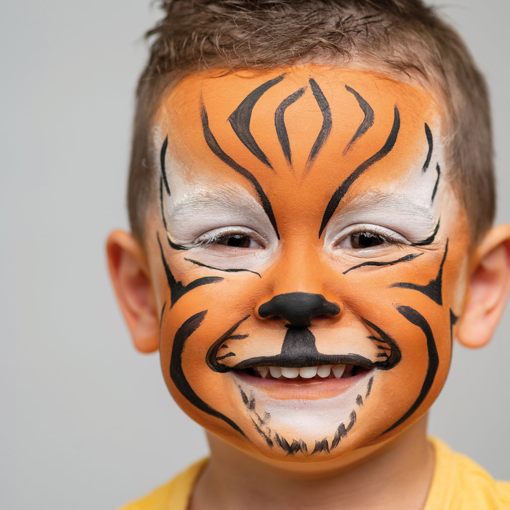 A cheerful child with a bold tiger face paint design in bright orange, black, and white.