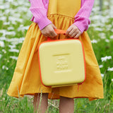 A child in a yellow dress holding the Plus-Plus BIG travel case outdoors in a field.