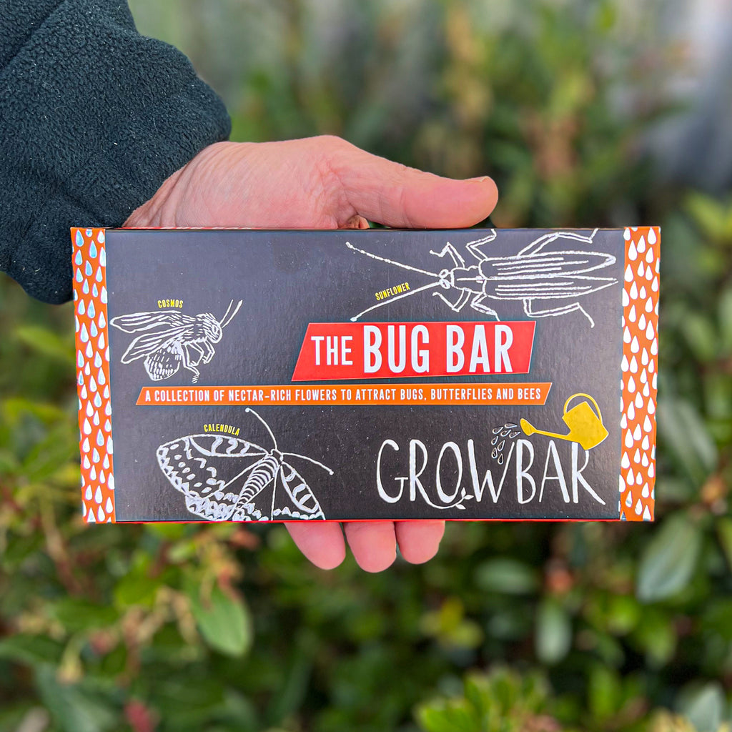 A black Growbar package labelled "The Bug Bar," featuring illustrations of insects and flowers, held in a hand against a leafy background.