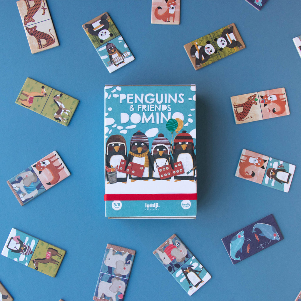 Londji Penguins & Friends Domino box with scattered game pieces – The game box in the centre, surrounded by various animal domino tiles.