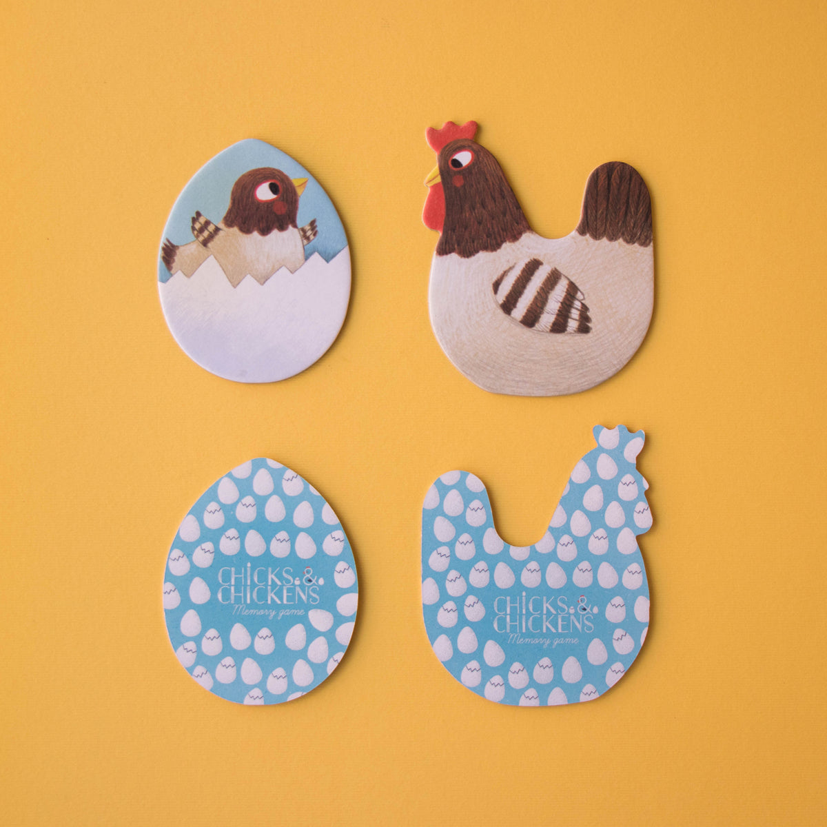 Four game pieces, including a hen, a chick, and the patterned backs of the memory game tiles.