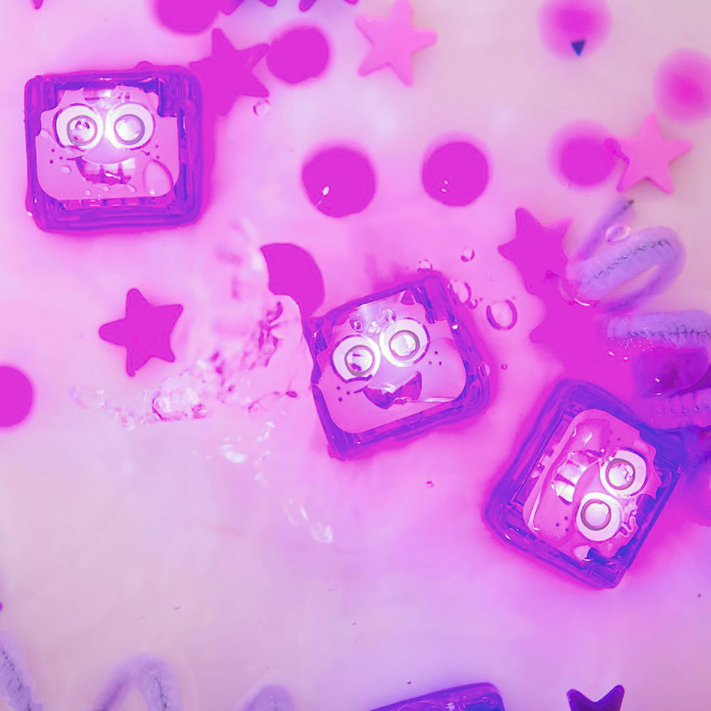 A set of glowing Lumi purple Glo Pals light-up cubes submerged in water, surrounded by pink stars and floating sensory elements.