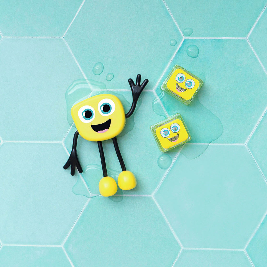  A yellow Glo Pals Alex character and two light-up cubes sitting on a light blue tiled surface with water droplets.
