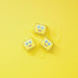 Three yellow Glo Pals light-up cubes on a vibrant yellow surface with water droplets.