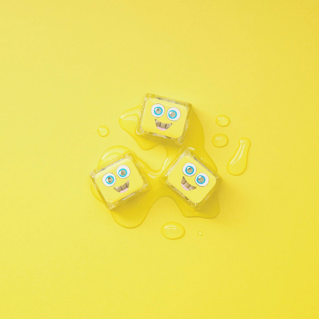 Three yellow Glo Pals light-up cubes on a vibrant yellow surface with water droplets.