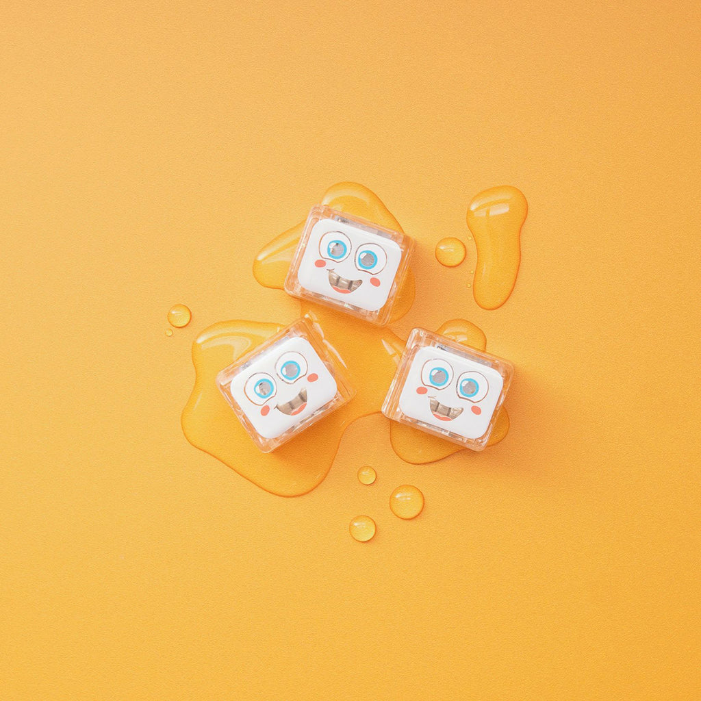 Three Glo Pals Party Pal light-up cubes resting on a bright orange surface with water droplets."