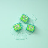 Three green Pippa Glo Pals light-up sensory cubes on a light blue surface with water droplets.