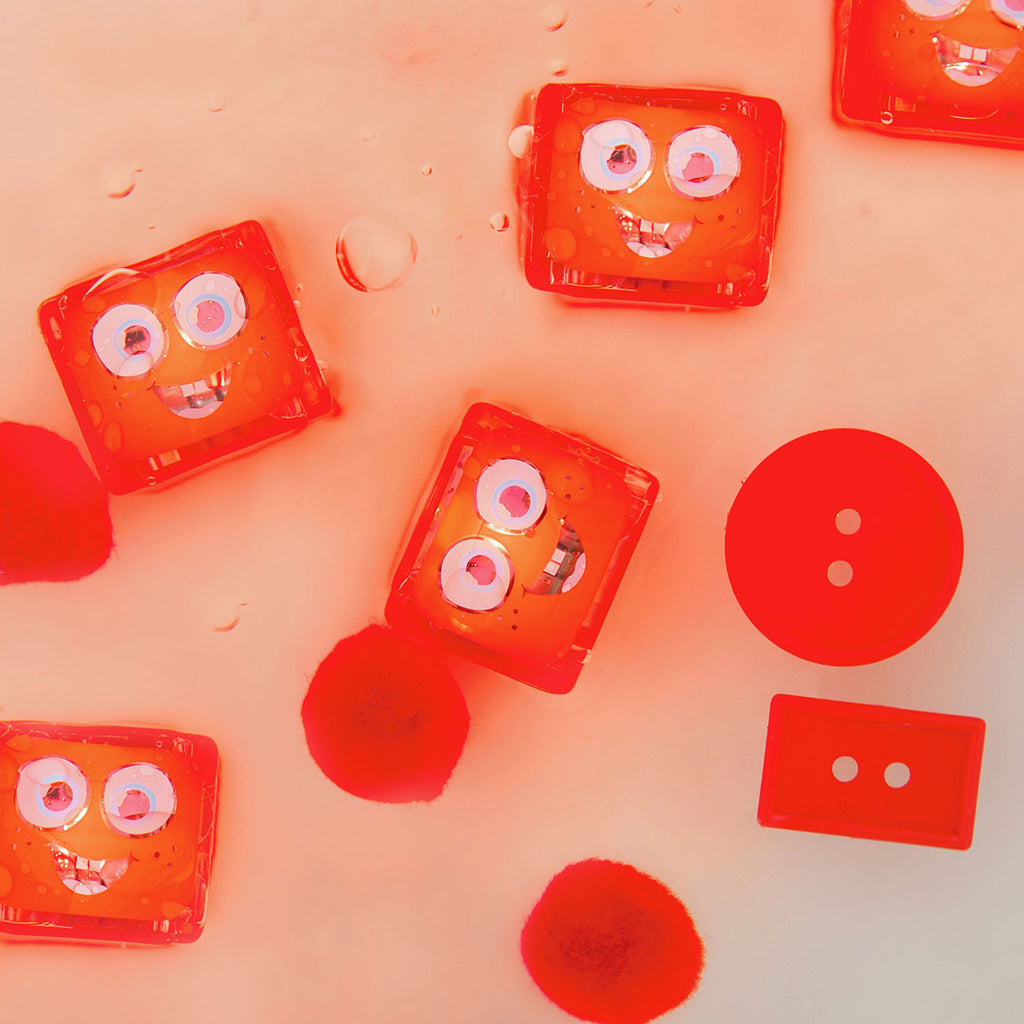 Water-activated Glo Pals Sammy light-up cubes floating in water with red pom-poms.