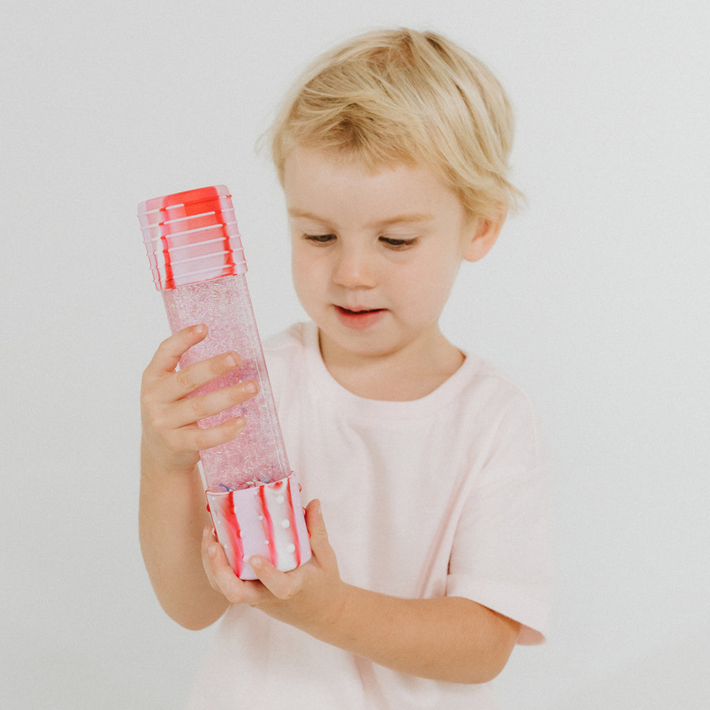 A young child wearing a light pink t-shirt holds and examines a candyland Jellystone Designs Calm Down Bottle.