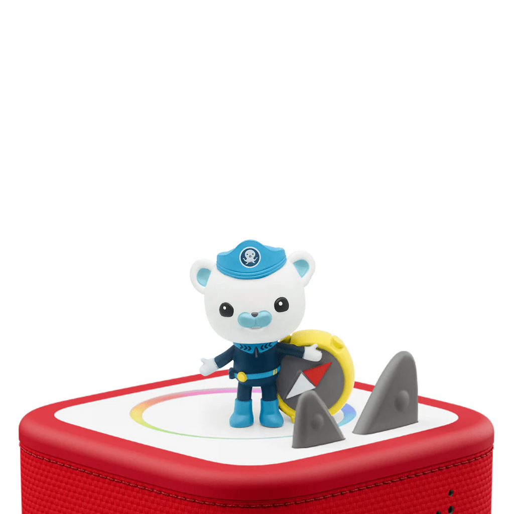A cute white polar bear figure wearing a blue sailor uniform and hat stands on a red platform. It holds a steering wheel and is next to two gray fins.