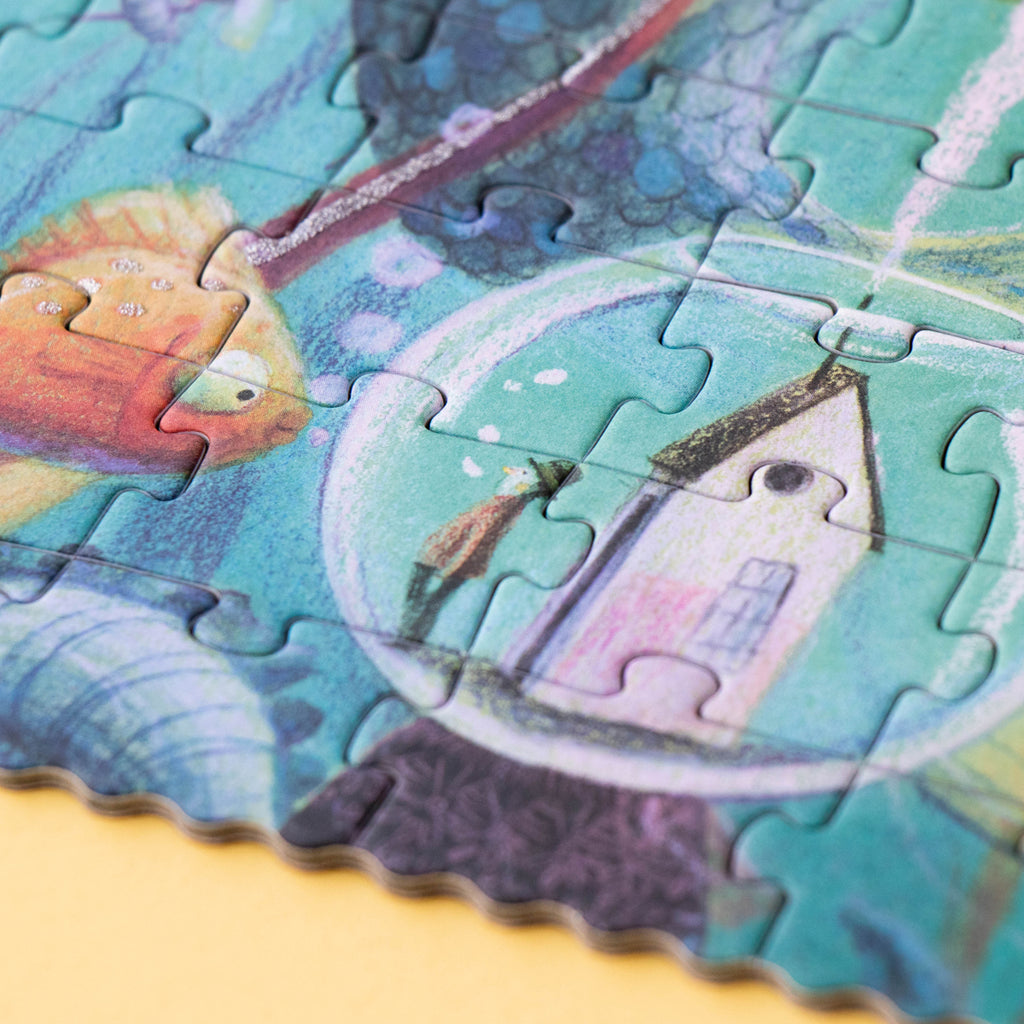 Close-up of a completed Londji My Mermaid puzzle, featuring a whimsical underwater scene with a tiny house inside a bubble, a curious fish, and glitter details.