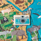 A close-up of an Animal Planet puzzle piece featuring a blue camera token placed on a vibrant illustration of the African savanna, surrounded by elephants, rhinos, and zebras.