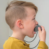 Child wearing a mustard yellow top, chewing on a Jellystone Designs robot pendant.