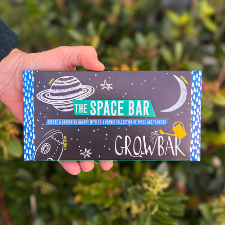 A black Growbar package labelled "The Space Bar," with cosmic illustrations of planets and stars, held against a green leafy background.