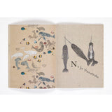 Children's book spread with sea creatures on the left and "N is for Narwhals" on linen-texture paper.