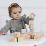 Toddler playing with and stacking wooden ABC learning blocks at a white table.