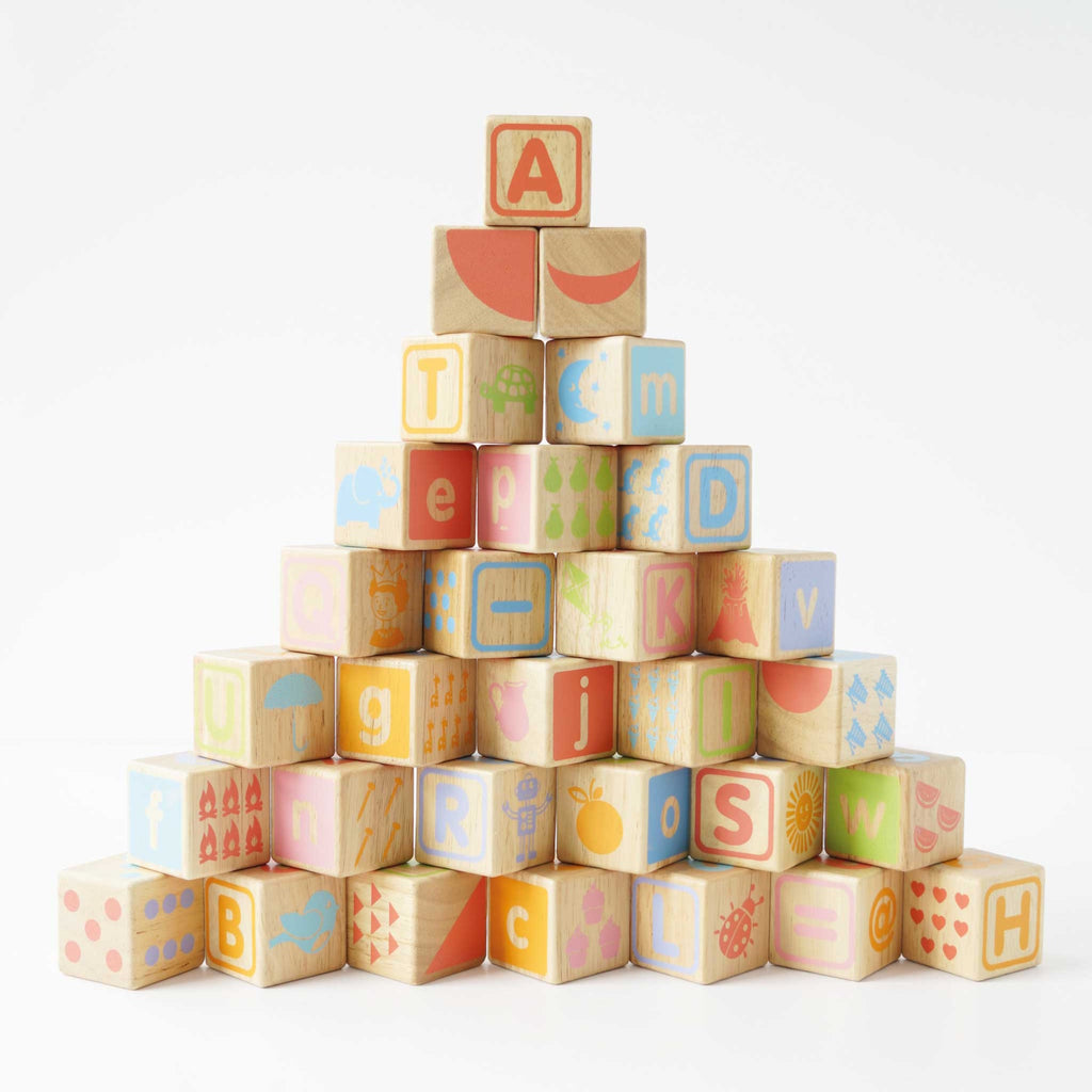 A colorful arrangement of wooden alphabet blocks featuring letters, numbers, and playful illustrations, stacked into a pyramid shape.