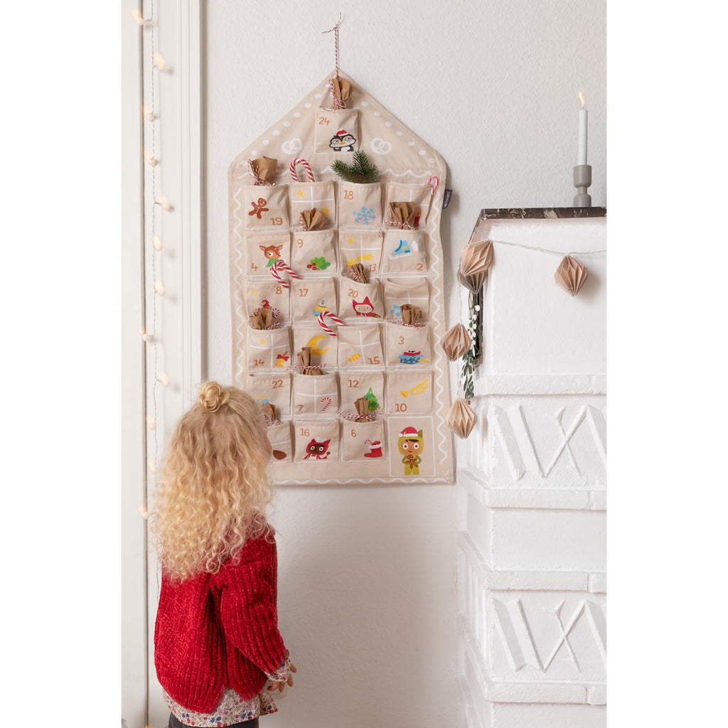 A festive fabric advent calendar with numbered pockets, featuring cheerful holiday-themed illustrations and a house-shaped design.