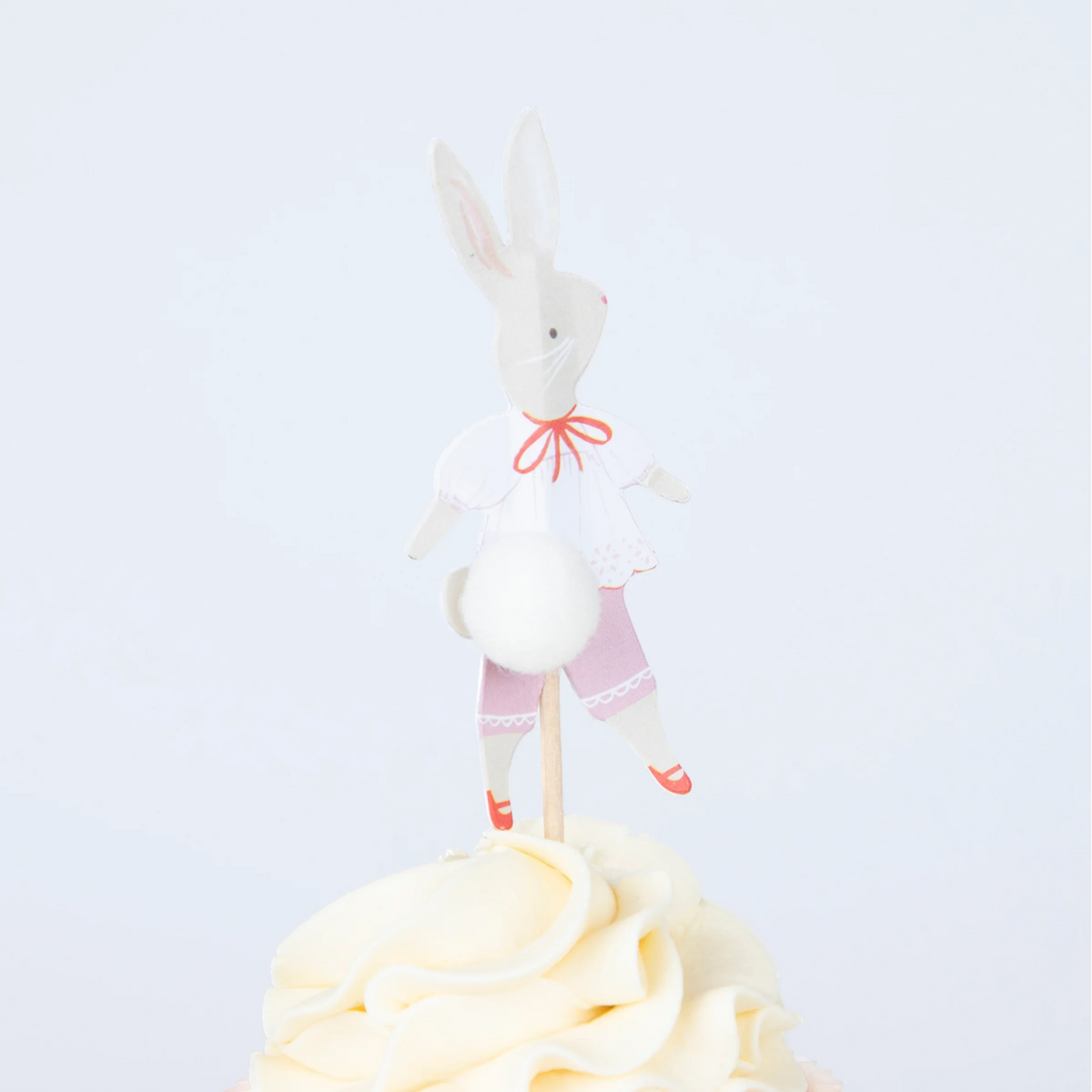 Close-up of a frosted cupcake topped with an illustrated bunny wearing pink trousers and a fluffy white pom-pom tail.