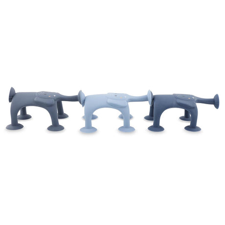 Three dog-shaped silicone kitchen sponges in varying shades of blue, featuring suction cup legs and cartoon-like faces, create a playful tone.
