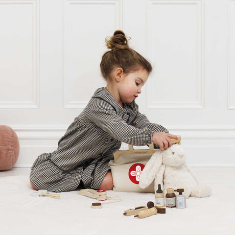 Young girl using a wooden brush on a plush white bunny next to a toy vet kit.